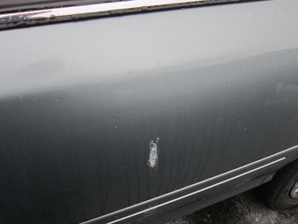 Close-up of a scratch on a gray car door, with some water droplets on the surface