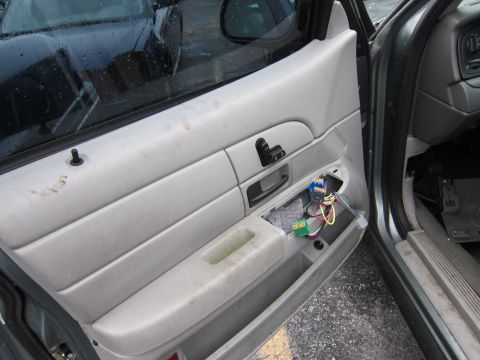 2001 Ford Crown Victoria - The interior door panel of a car shows exposed wiring and window controls, indicating potential damage or repair.