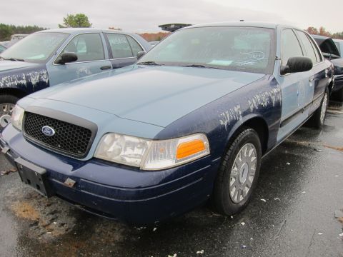 2001 Ford Crown Victoria - Two Ford Crown Victorias are parked in a lot, one with a two-tone paint scheme.