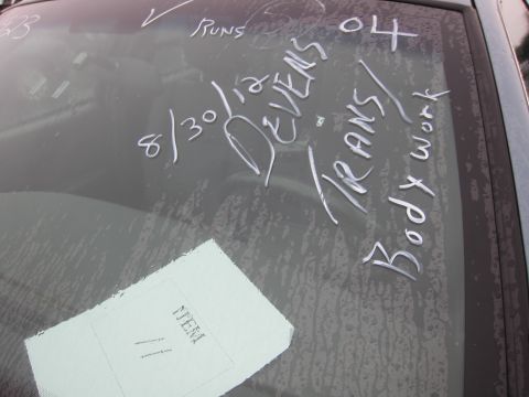 2001 Ford Crown Victoria - Chalk markings on a vehicle's windshield indicate 'Body work' and dates, with a paper tag visible.