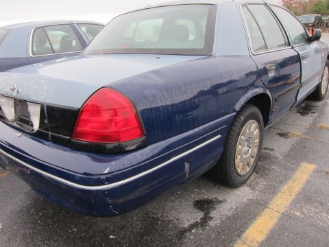 2001 Ford Crown Victoria - Two Ford Crown Victorias are parked outside on a wet day. The closest car has a two-tone paint job.