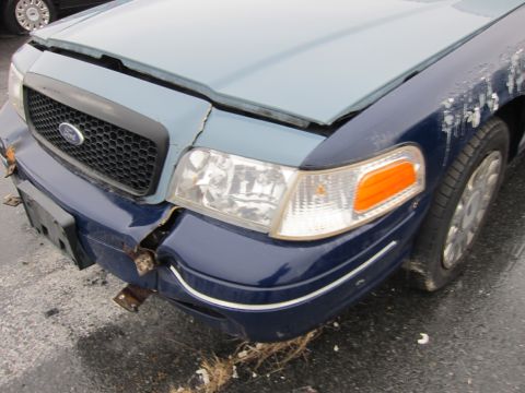 2001 Ford Crown Victoria - The front of a 2001 Ford Crown Victoria shows significant damage to the bumper and hood, with a two-tone paint scheme.
