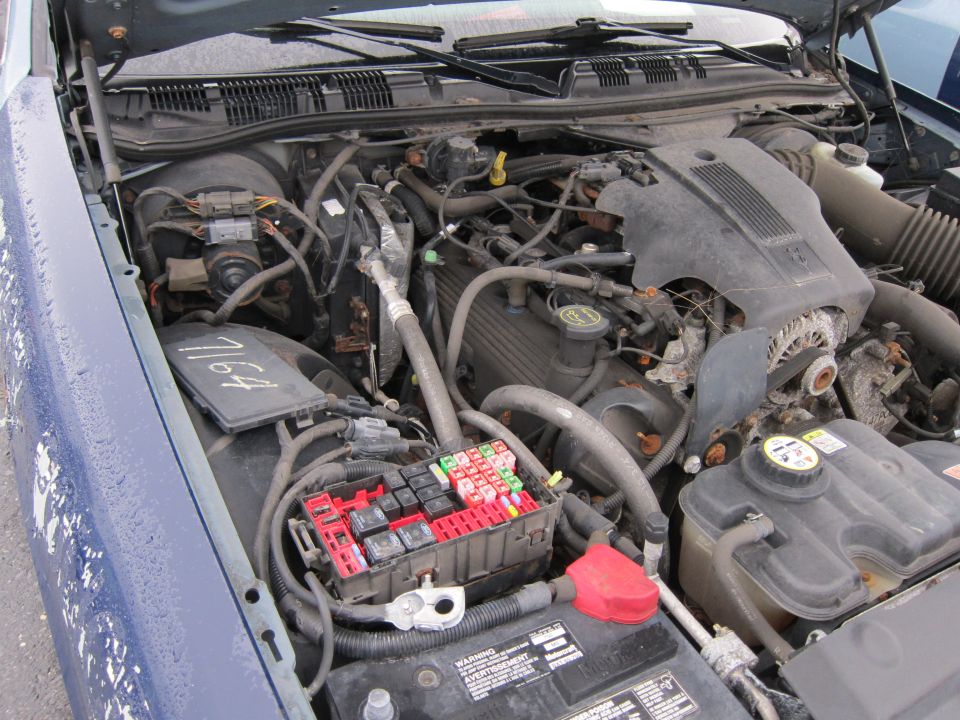Engine bay of a 2001 Ford Crown Victoria, showing the engine, fuse box, battery, and various hoses and wires