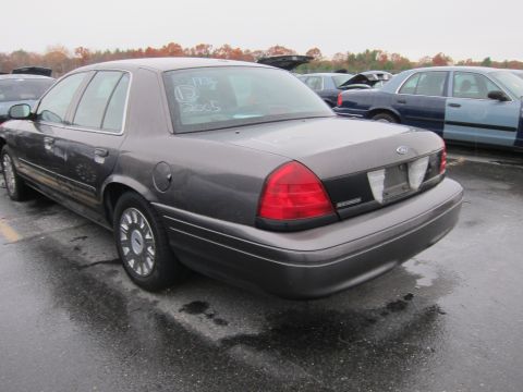 2001 Ford Crown Victoria - A dark gray Ford Crown Victoria is parked in a lot with other vehicles under an overcast sky.