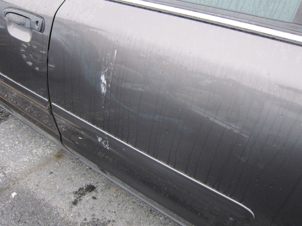 Gray car door with white paint scuffs and streaks, showing a door handle and part of a window trim