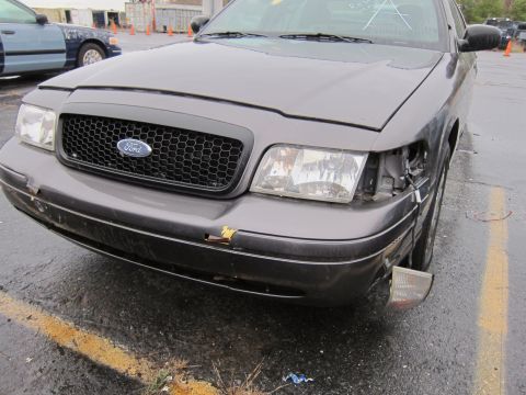 2001 Ford Crown Victoria - This 2001 Ford Crown Victoria shows damage to its front bumper and headlight assembly, with another vehicle visible in the background.