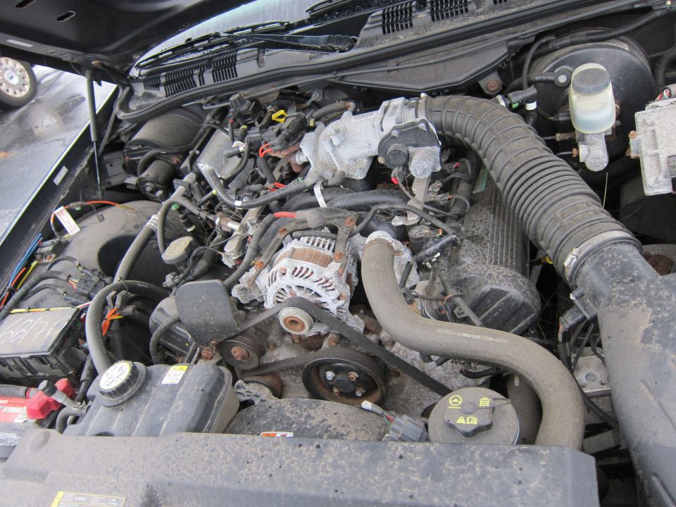 Engine bay with hoses, belts, and alternator visible. Some text on a fuse box
