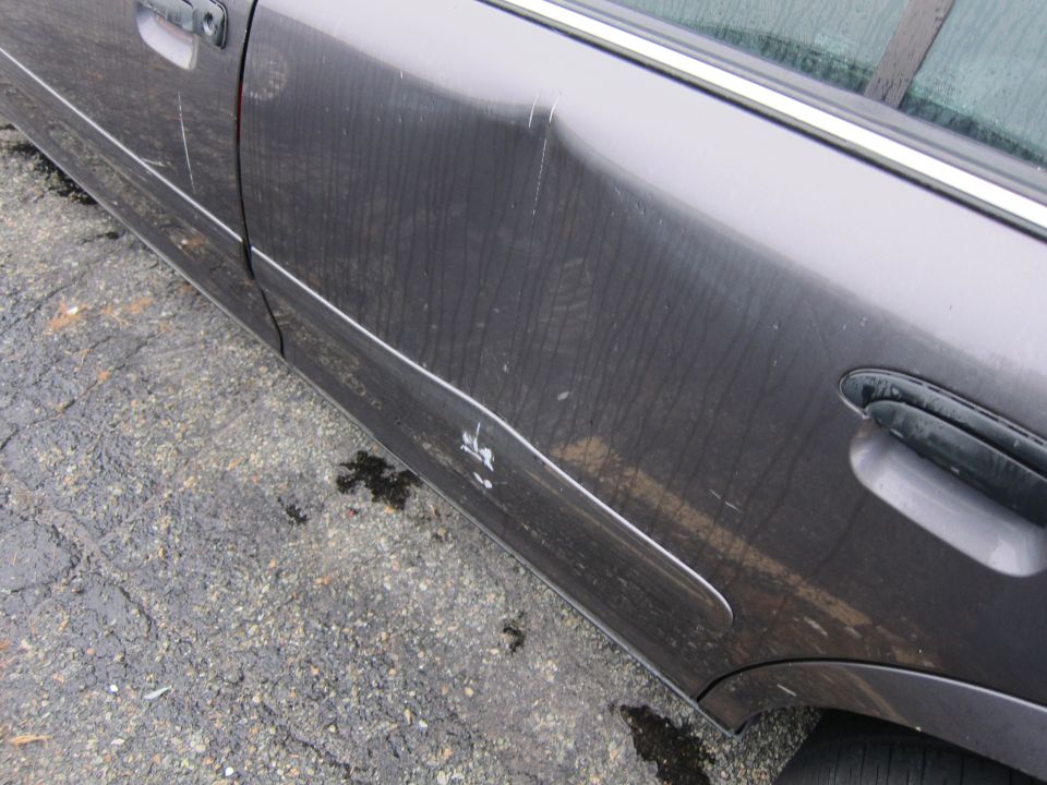 Dark gray car door with a large dent and white paint transfer near the body line