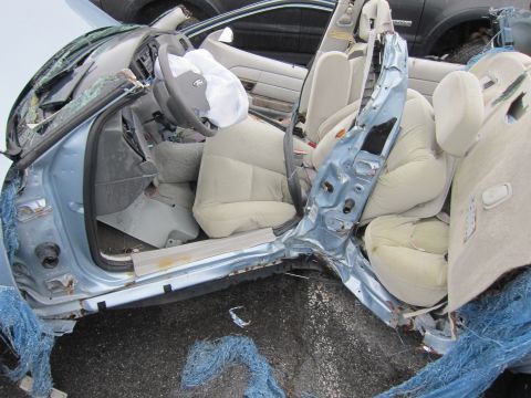 2001 Ford Crown Victoria - The interior of a heavily damaged 2001 Ford Crown Victoria, with airbags deployed and the driver's side door crushed inward.