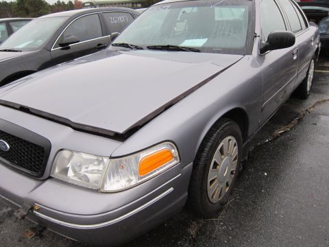2001 Ford Crown Victoria - A silver 2001 Ford Crown Victoria is parked on wet asphalt, with its hood slightly open.