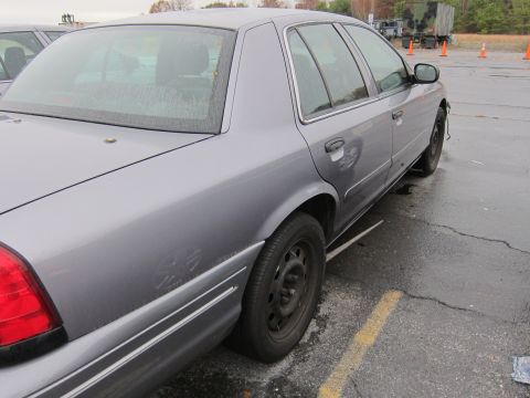 2001 Ford Crown Victoria - Side view of a gray 2001 Ford Crown Victoria, parked on wet asphalt with another vehicle visible.