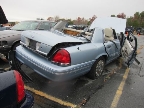 2001 Ford Crown Victoria - A light blue 2001 Ford Crown Victoria sits in a lot with its roof heavily damaged and doors ajar, indicating significant wear or damage.