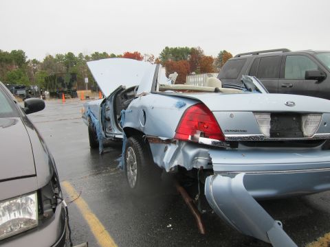 2001 Ford Crown Victoria - Heavily damaged 2001 Ford Crown Victoria convertible sits in a lot with its hood open.