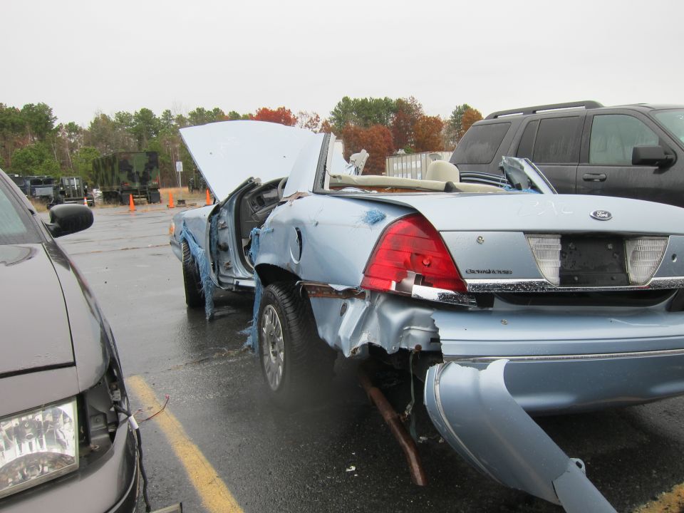2001 Ford Crown Victoria convertible, rear end heavily damaged, hood open. Another car is parked to the left