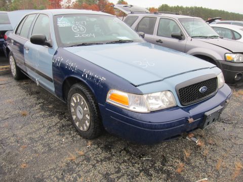 2001 Ford Crown Victoria - A two-tone Ford Crown Victoria sits in a lot with other vehicles, showing some handwritten markings on its body.
