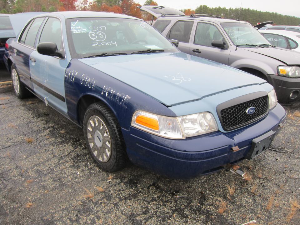 Ford Crown Victoria with mismatched blue panels, some writing on windshield and hood. Another SUV is parked behind it