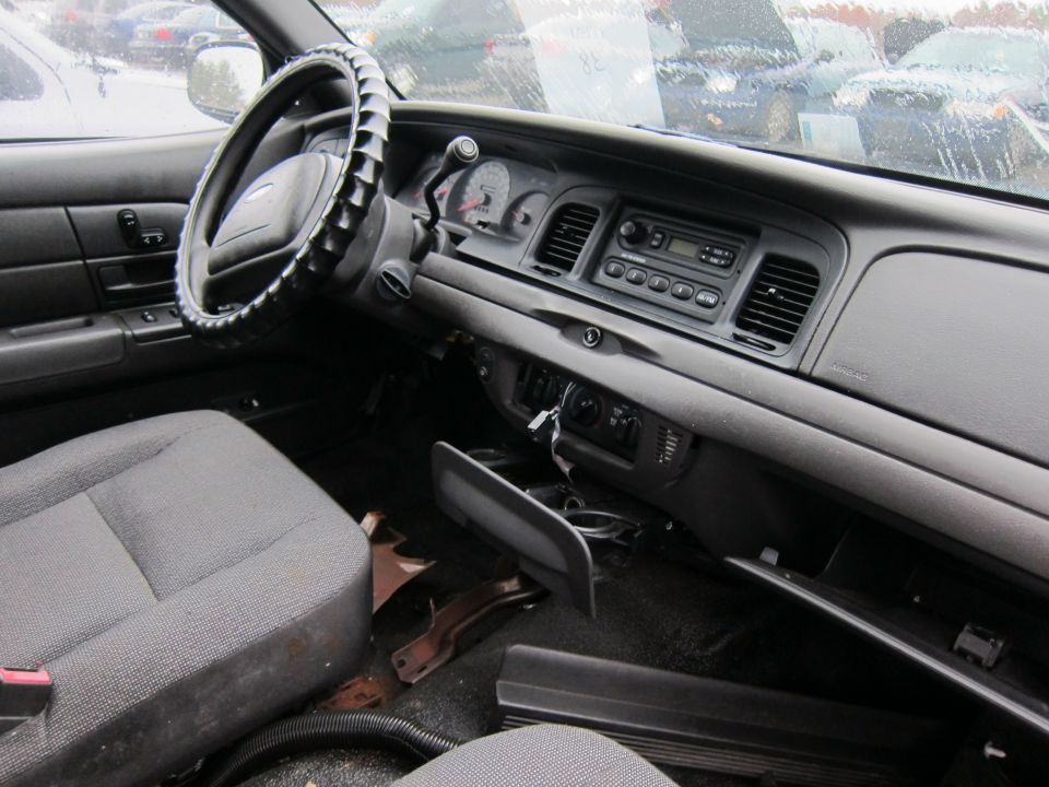 2001 Ford Crown Victoria interior, driver's side view, worn gray fabric seats, cracked dashboard, aftermarket steering wheel cover