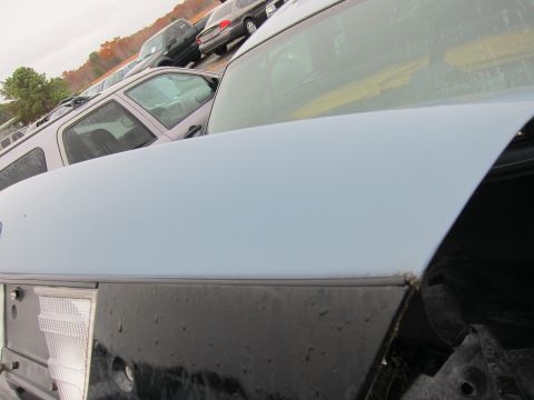 2001 Ford Crown Victoria - Close-up of a light blue car's trunk and rear quarter panel, with other vehicles visible in the lot.