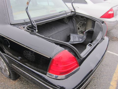 2001 Ford Crown Victoria - The rear of a black 2001 Ford Crown Victoria is shown with its trunk open and a flat tire on the rear passenger side.