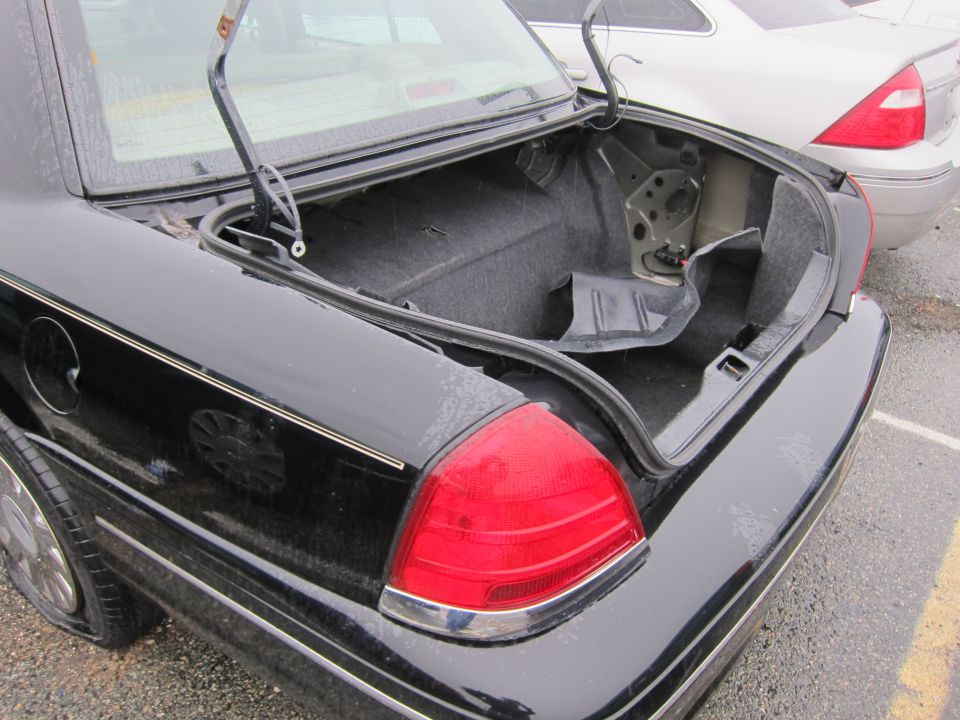 Black 2001 Ford Crown Victoria rear with open trunk and flat tire