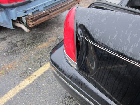 2001 Ford Crown Victoria - The rear of a black 2001 Ford Crown Victoria is visible, with a damaged blue vehicle in the background.