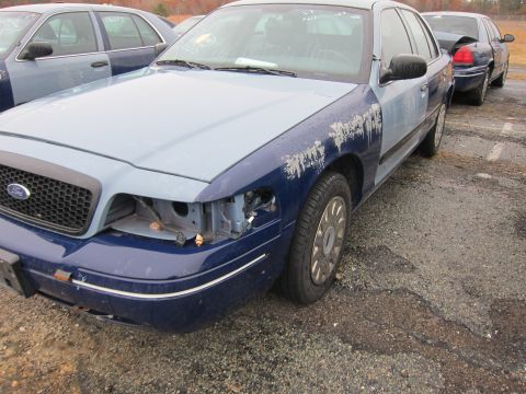 2001 Ford Crown Victoria - A blue and light blue Ford Crown Victoria is parked in a lot with other vehicles, showing damage to the front passenger side.