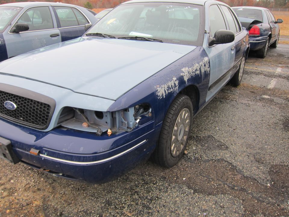 Blue and light blue Ford Crown Victoria with missing headlight and peeling paint on fender