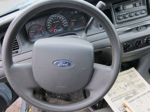2001 Ford Crown Victoria - Interior view of a 2001 Ford Crown Victoria, showing the steering wheel, dashboard, and a newspaper on the floor.