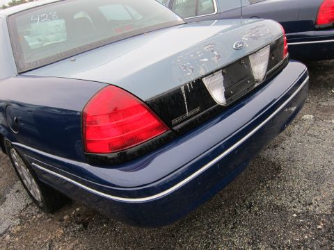 2001 Ford Crown Victoria - The rear of a blue 2001 Ford Crown Victoria Police Interceptor is shown, with a faded light blue trunk lid and visible police markings.