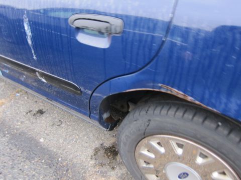 2001 Ford Crown Victoria - The rear passenger side of a blue sedan shows significant rust and body damage.