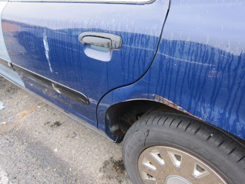 2001 Ford Crown Victoria - A blue sedan's rear door and wheel well show signs of rust and damage.