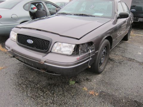 2001 Ford Crown Victoria - A damaged 2001 Ford Crown Victoria sits in a lot with its hood and driver's side door open.