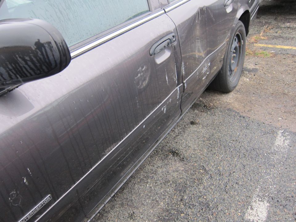 Dark sedan side view, showing damage to the rear door and fender. The word INTERCEPTOR is visible on the lower body trim