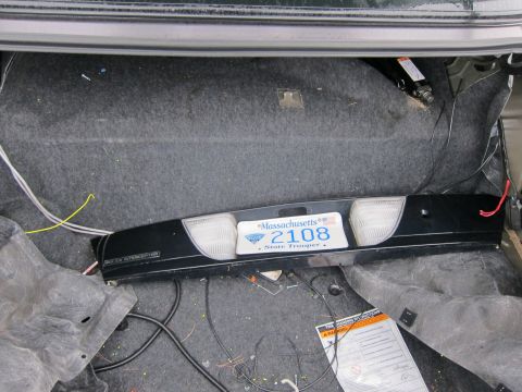 2001 Ford Crown Victoria - The trunk interior of a vehicle displays a black taillight assembly and a Massachusetts State Trooper license plate.