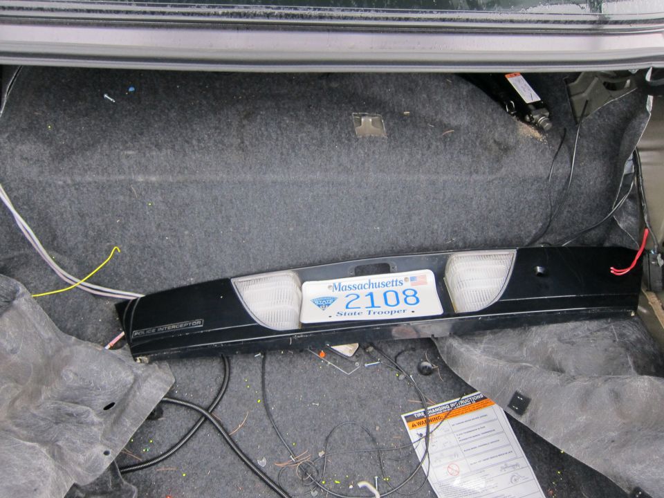 Trunk interior showing a black taillight assembly with a Massachusetts State Trooper license plate