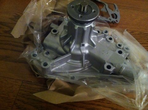 1978 Ford Bronco - A new water pump, still in its packaging, rests on a wooden surface.
