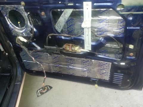 1994 Ford Bronco - The interior of a car door is shown with sound dampening material applied to the inner panel and exposed wiring for the window mechanism.