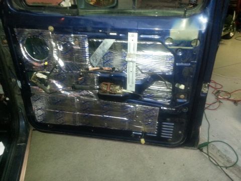 1994 Ford Bronco - Interior of a blue tailgate or rear door panel removed to show foil sound-deadening mat, wiring harness, latch and regulator mechanism in a…