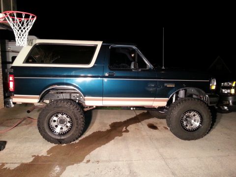 1995 Ford Bronco - A teal 1995 Ford Bronco with a white removable top sits on a concrete driveway at night.