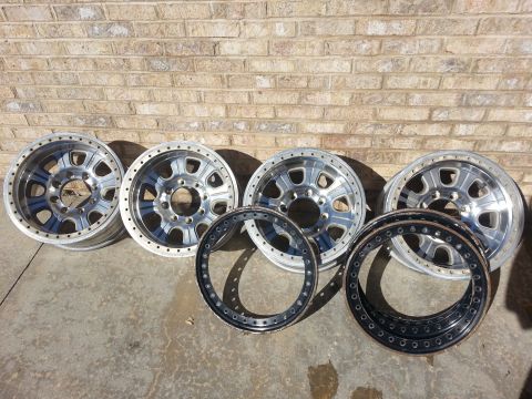 1995 Ford Bronco - Four aluminum wheels and two beadlock rings are displayed on a concrete surface in front of a brick wall.