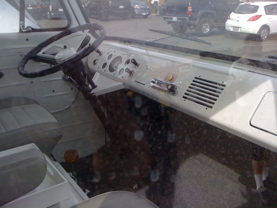 White van interior with a two-spoke steering wheel, dashboard with gauges and radio, and cloth seats