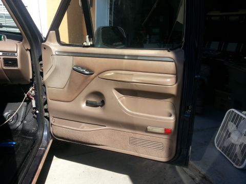 1994 Ford Bronco - The interior door panel of a vehicle shows the armrest, window controls, and a storage pocket.