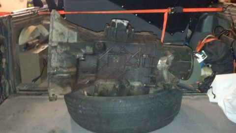 1995 Ford Bronco - A transmission unit is shown resting on a tire, possibly inside a vehicle's cargo area.