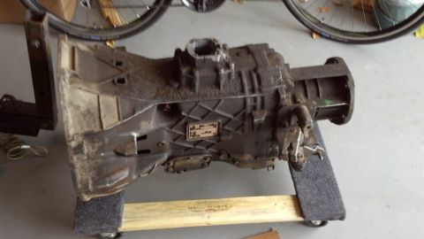 1995 Ford Bronco - A transmission part is shown, resting on a wooden stand. A metal tag is visible on the side of the part.