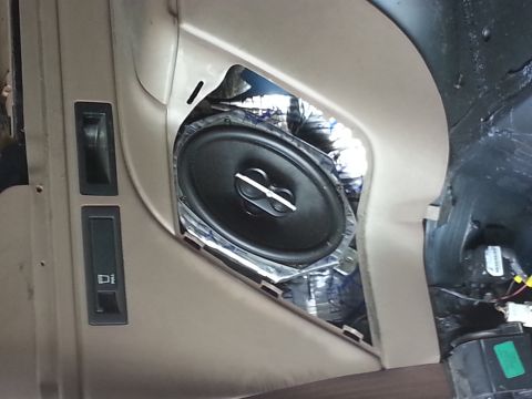 1994 Ford Bronco - A close-up view of a speaker installed in a vehicle's door panel, with insulation material showing.