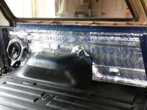 1994 Ford Bronco - The interior of a vehicle shows sound dampening material and a speaker being installed in the rear panel.