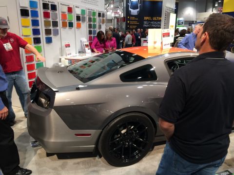 2013 Ford Mustang - A gray sports coupe is displayed at an auto show, with attendees observing the vehicle.