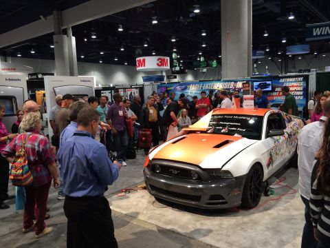 2013 Ford Mustang - A customized 2013 Ford Mustang GT is displayed at an event, a unique orange and white paint scheme with graphics.