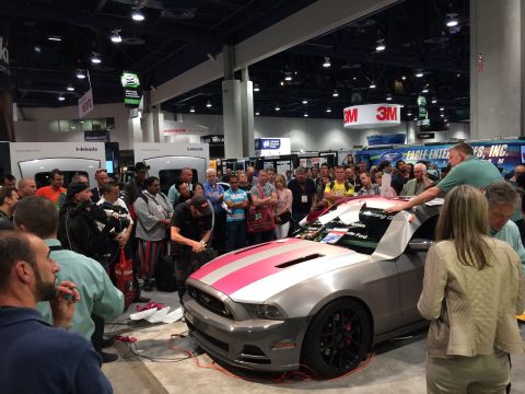 2013 Ford Mustang - A group of people gather around a silver Ford Mustang with pink and silver racing stripes on the hood, as a man applies a graphic to the ca…