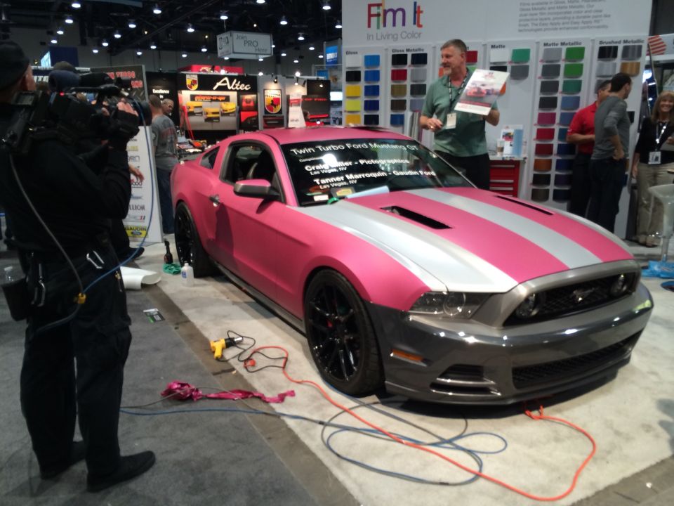 Pink and silver striped Ford Mustang GT at a trade show with a cameraman.